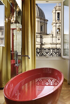 A red bathtub in a room with a view of a historic building through a window. - Lifestyle Suites Rome (Rome)
