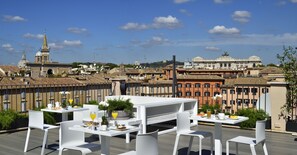 A rooftop terrace with white tables and chairs, a dining setup with plates, glasses, and a potted plant. - Lifestyle Suites Rome (Rome)