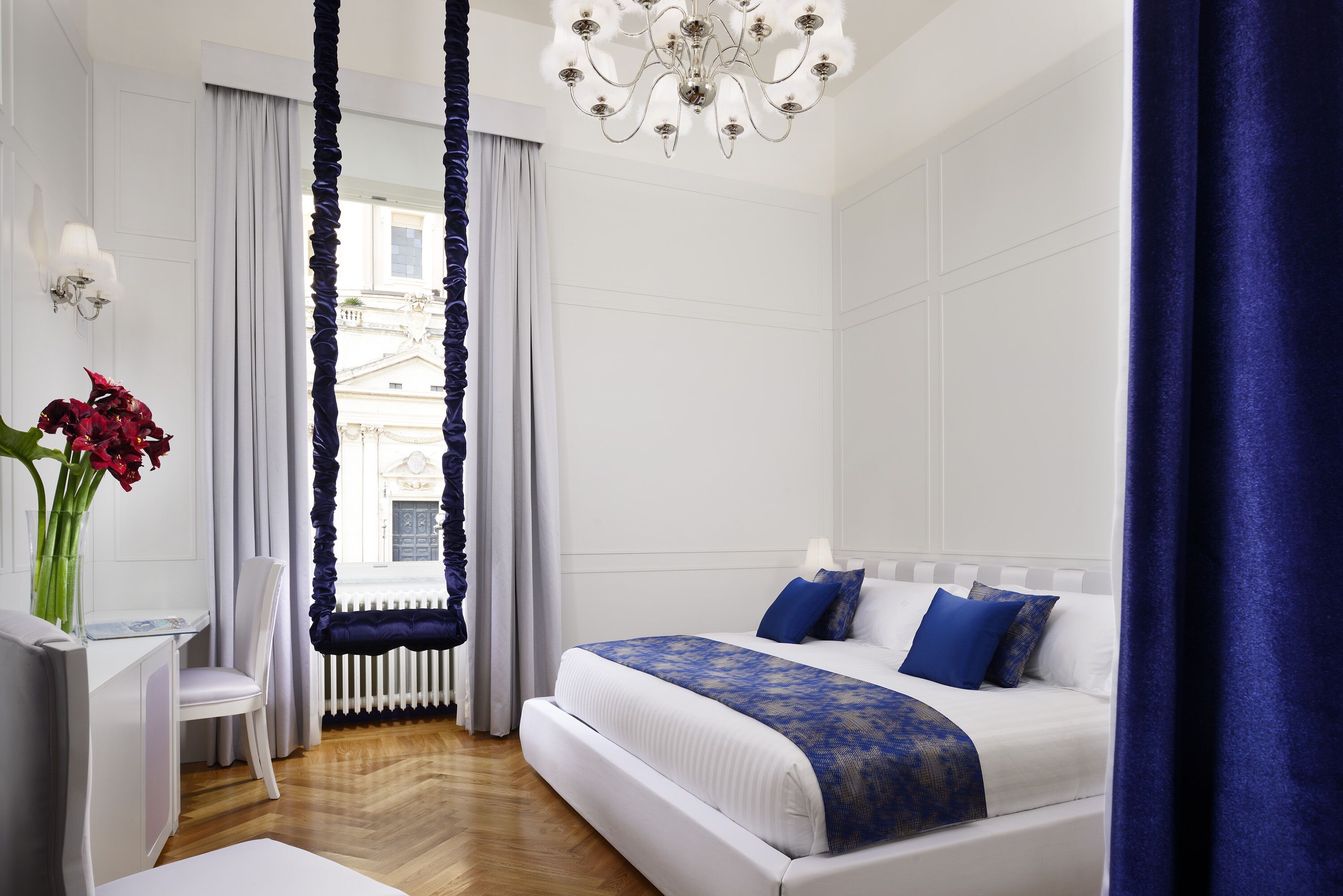 Un dormitorio moderno con una cama grande, una araña, vistas de la ciudad y una ventana con cortinas.