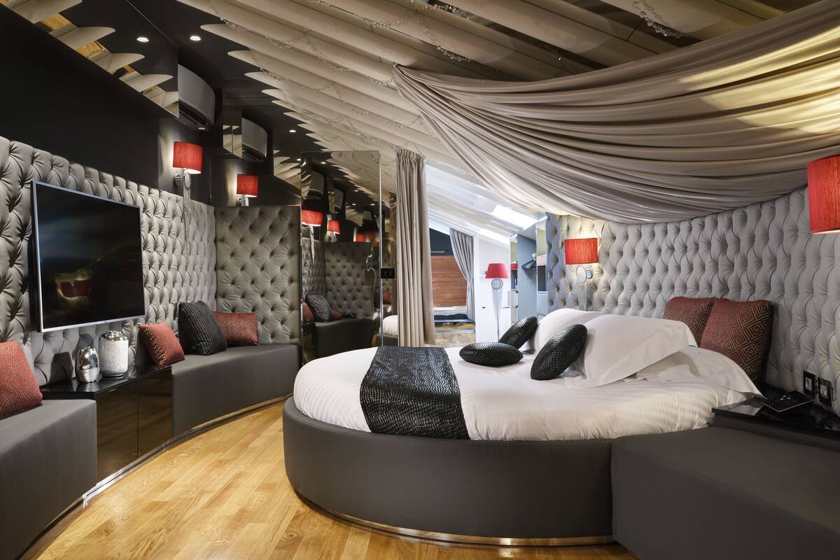 A modern bedroom with a round bed, tufted headboard, and a large flat-screen TV.