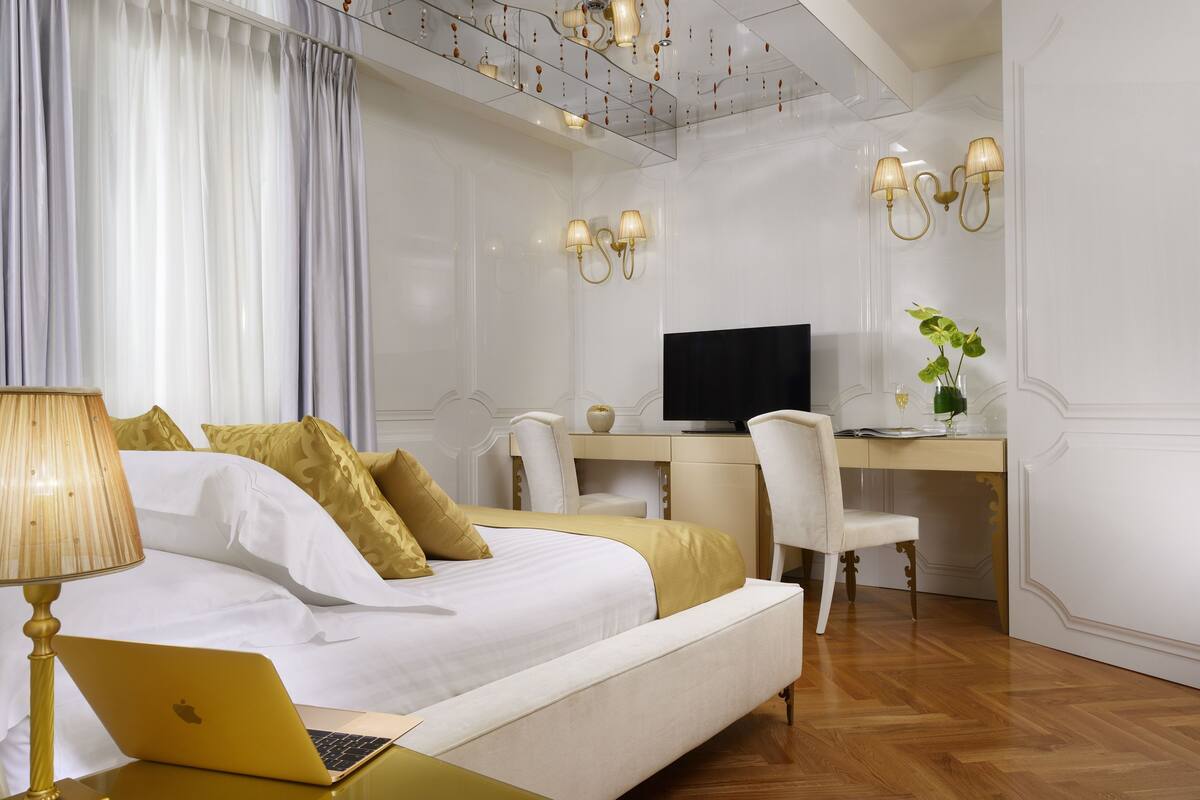 A bedroom with a bed, a desk, a chair, a television, and a laptop.