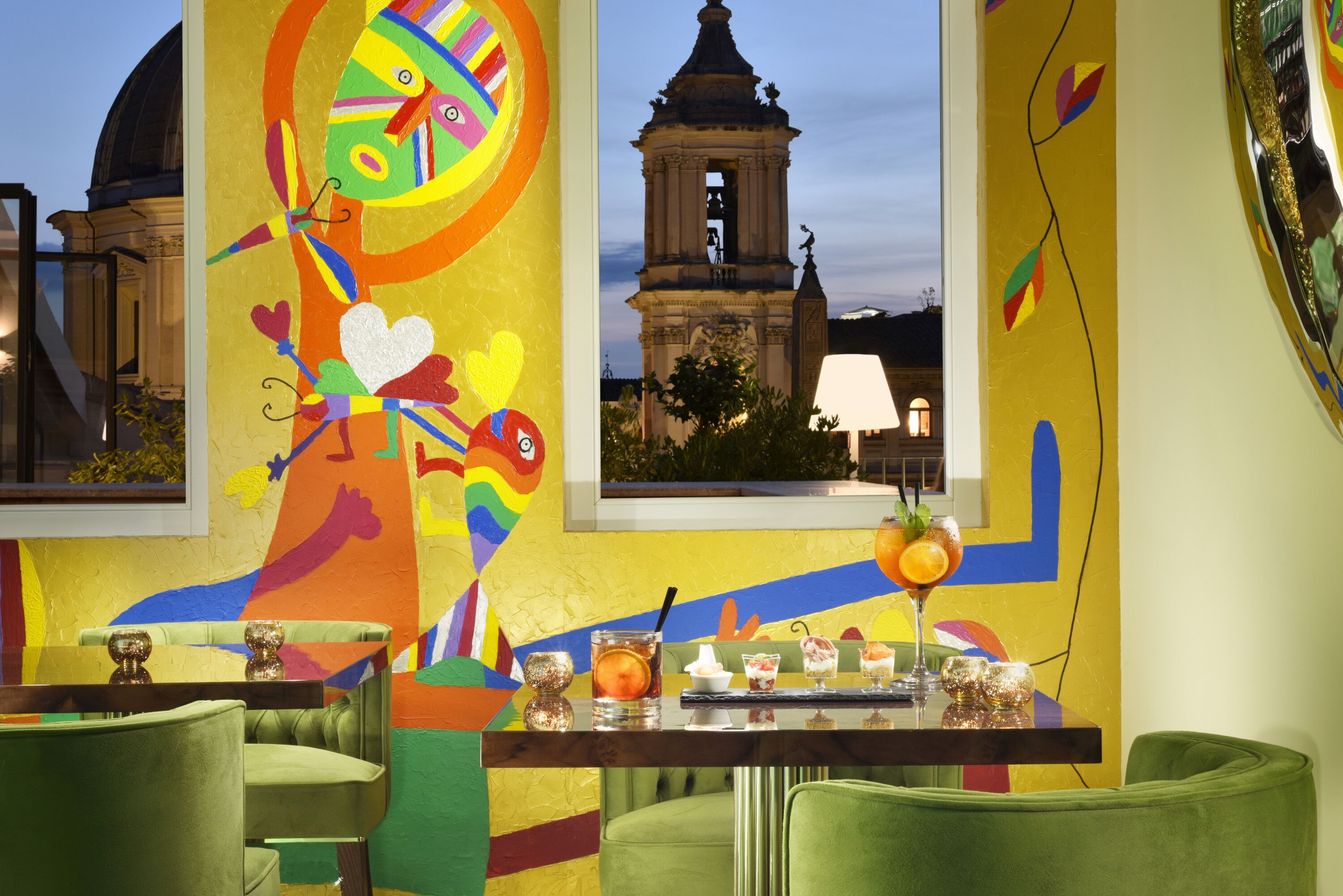 Un interior vibrante con murales coloridos, vistas a una torre histórica y una zona de bar con bebidas.
