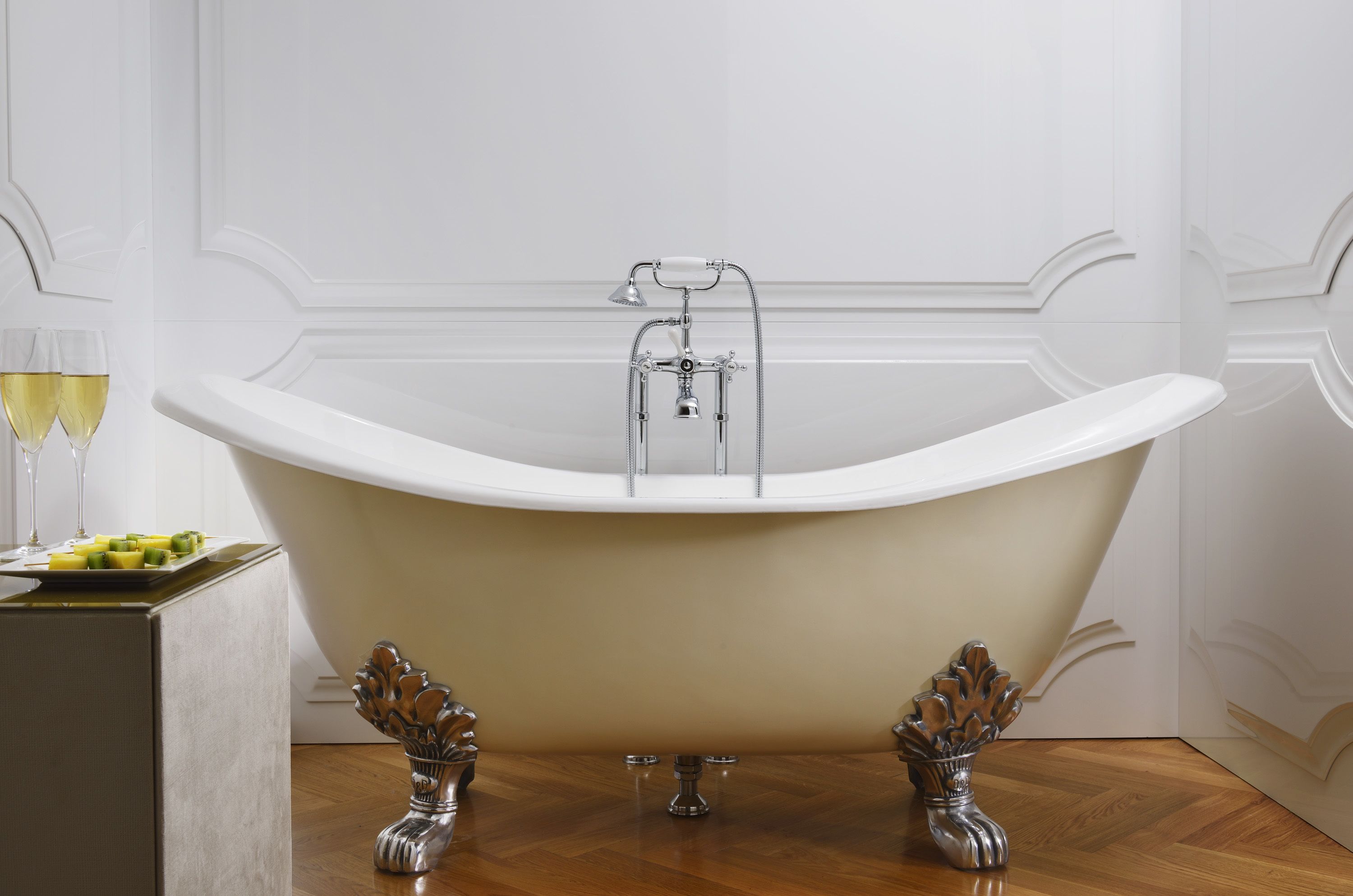 Una bañera independiente con ducha, una mesita con una bandeja de frutas y vasos, y jarrones decorativos en el suelo.