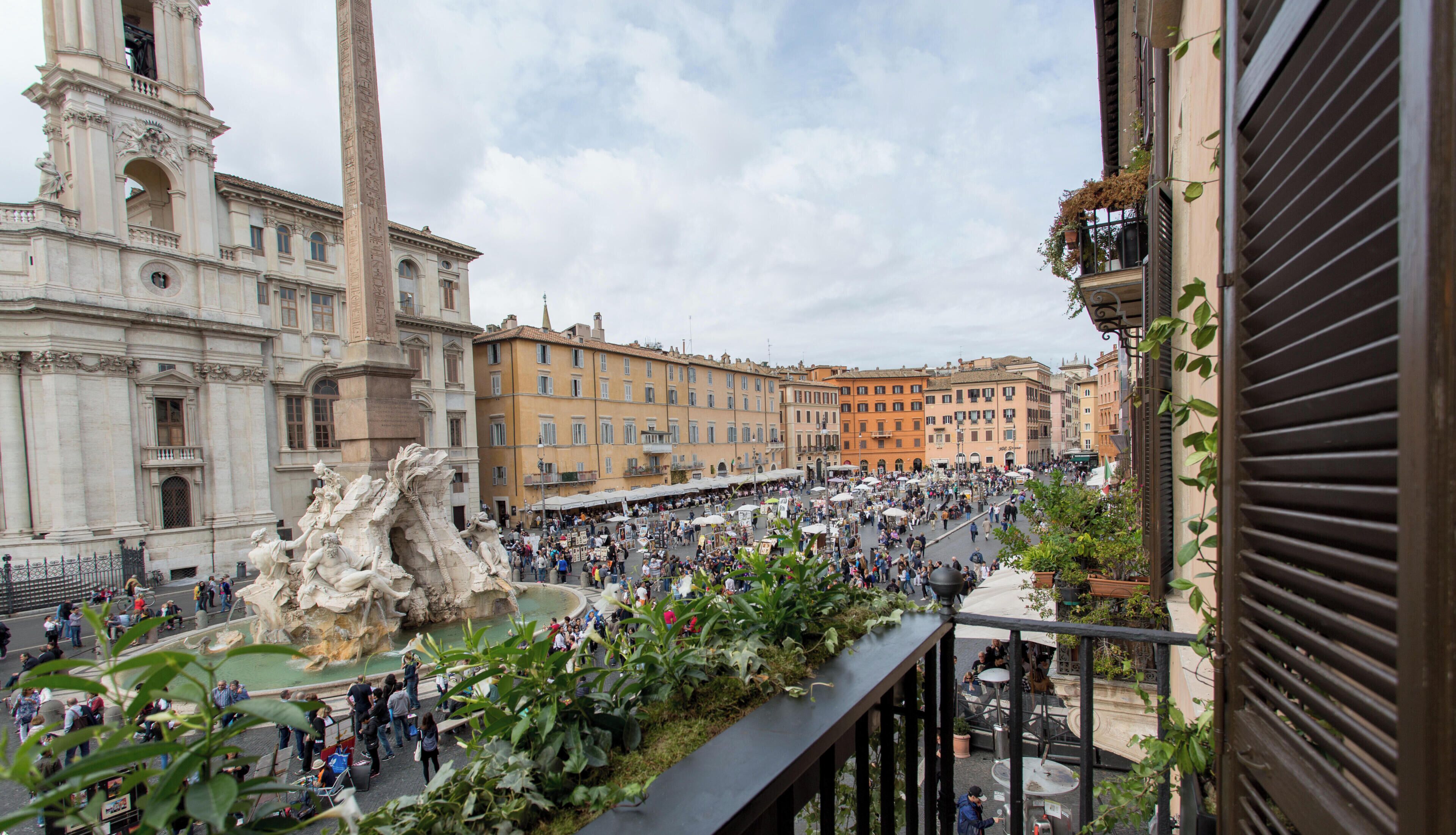 A bustling square with a fountain, historic buildings, and a crowd of people.