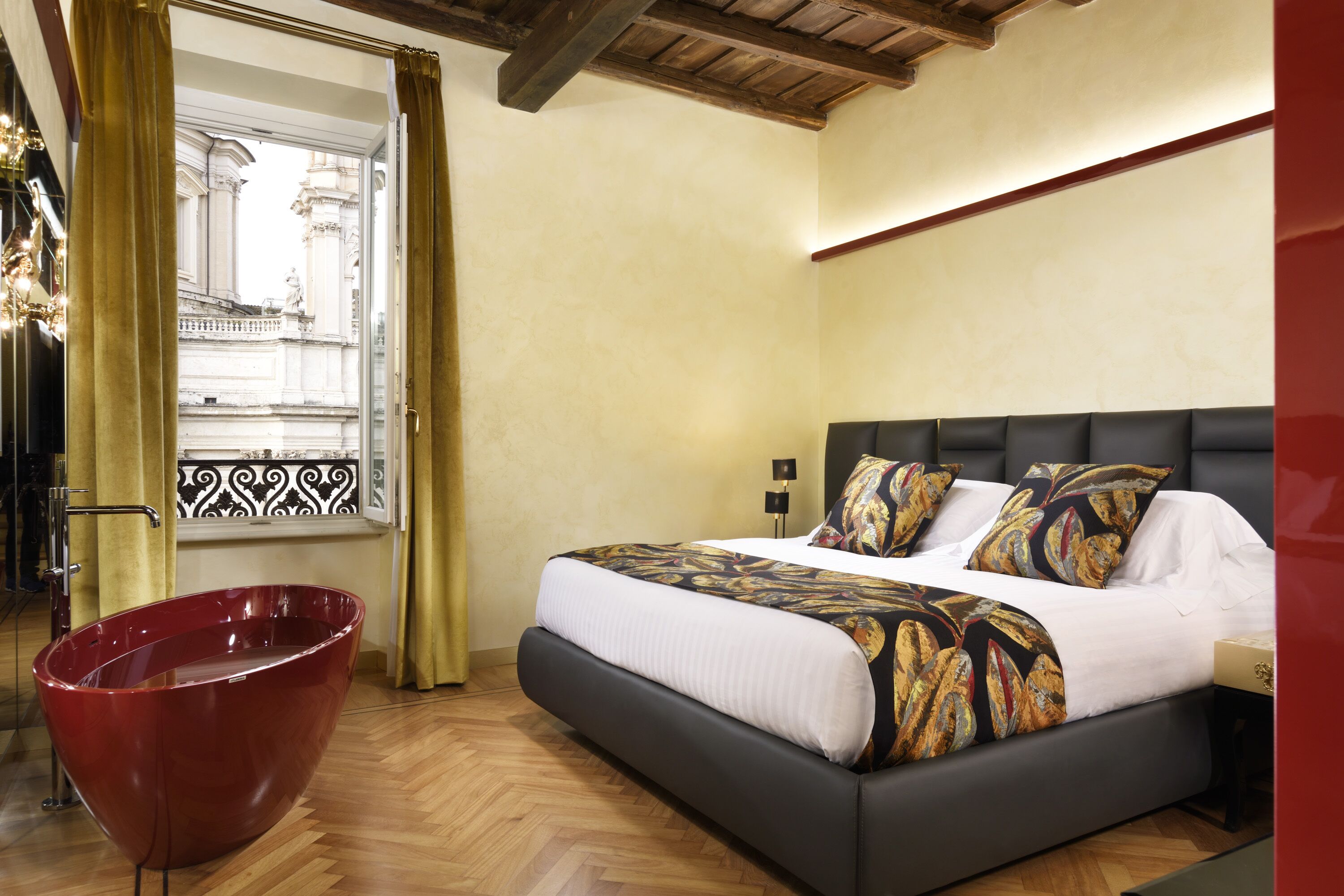 A bedroom with a large bed, a red bathtub, and a window with a view of a building.