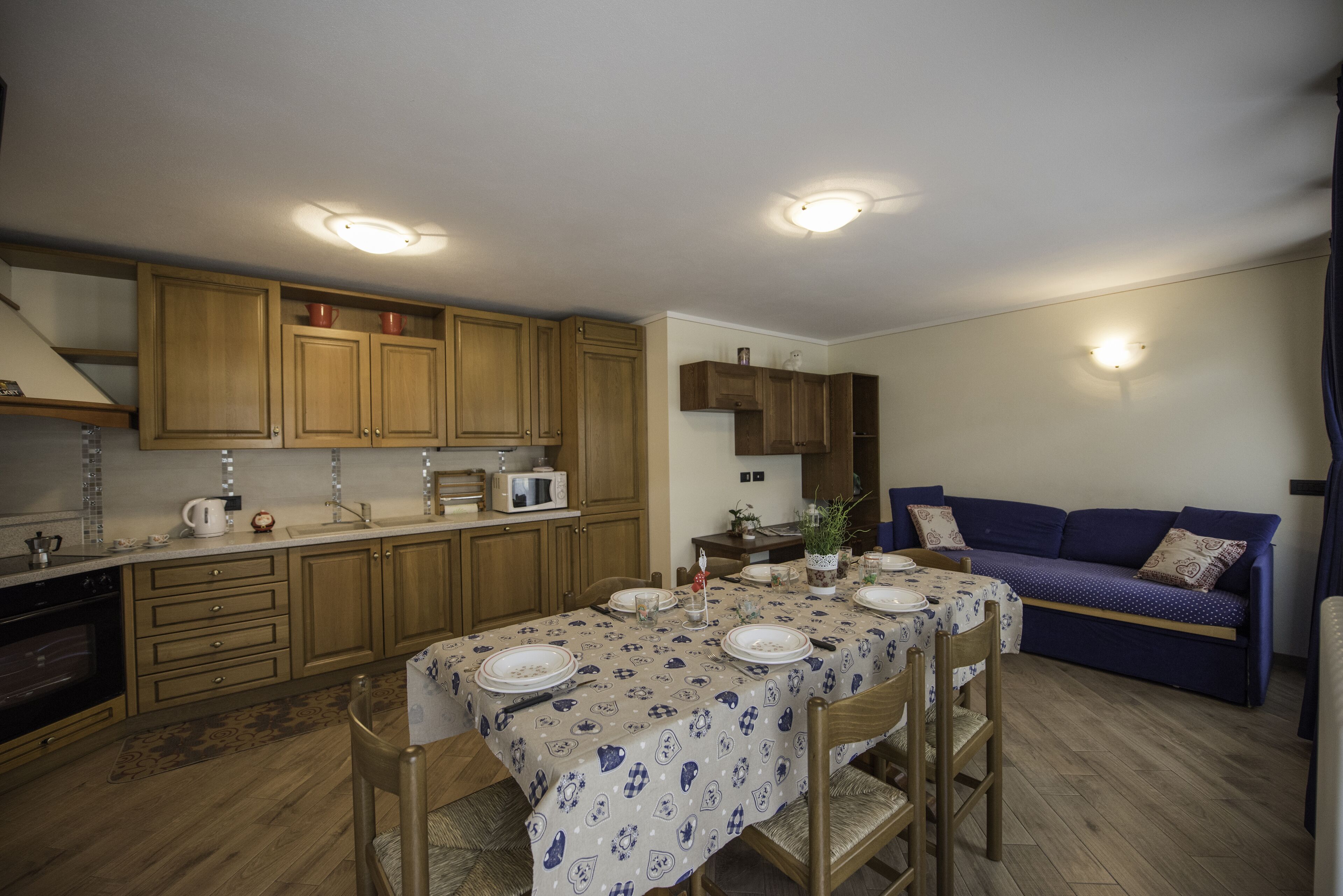 Una cocina compacta con armarios de madera, una mesa de comedor preparada para cuatro personas y un sofá azul en el área de estar contigua.