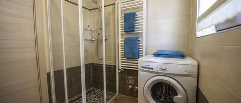A bathroom with a glass-enclosed shower, a built-in washing machine, and a towel rack with two towels.