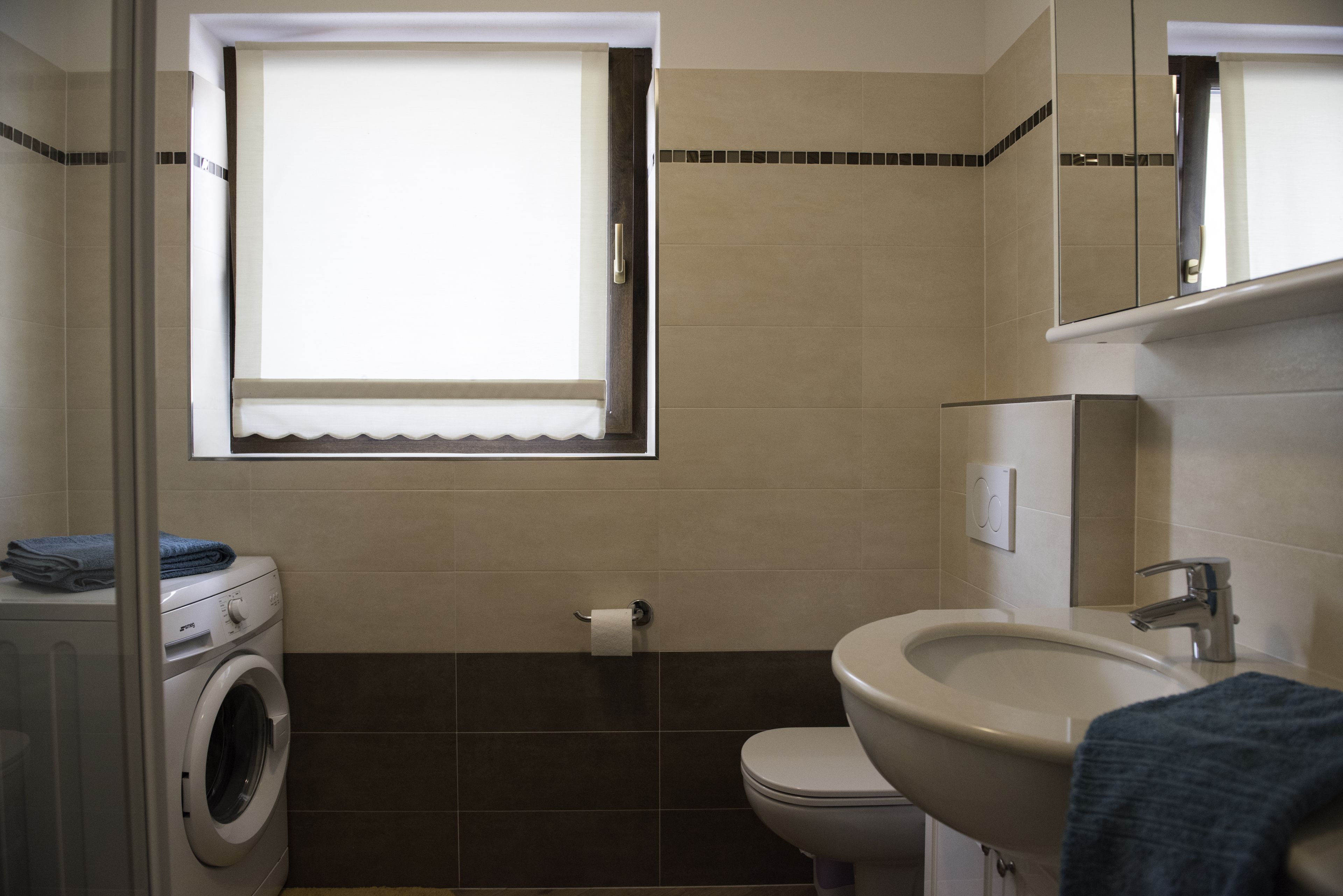A bathroom with a washing machine, toilet, sink, and a window with a view.