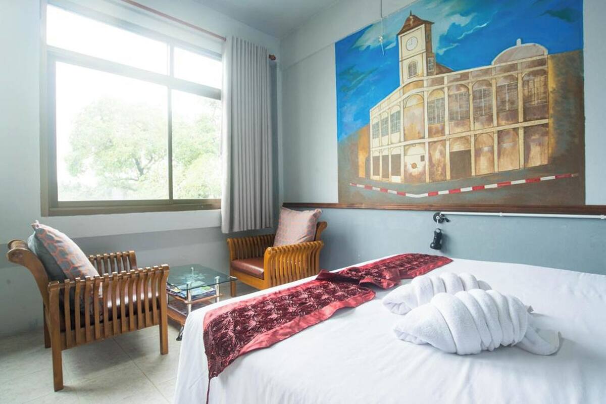 Una habitación de hotel con una cama, una silla, una mesa y un cuadro grande en la pared.