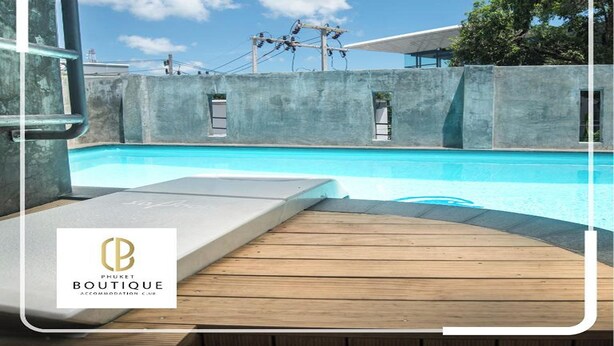 A pool area with a wooden deck, concrete walls, and a clear blue sky.