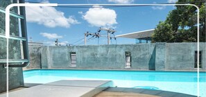 A pool area with a wooden deck, concrete walls, and a clear blue sky. - Beehive Phuket Old Town - Hostel (Phuket)