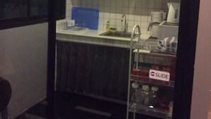 A small kitchen with white cabinets, a sink, and a dishwasher. There is a blue cutting board and a metal rack with jars. - Hubb Hostel Phuket Airport (Sa Khu)