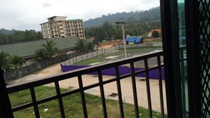 A view from a balcony with a metal railing, overlooking a grassy area with a building in the background. - Hubb Hostel Phuket Airport (Sa Khu)