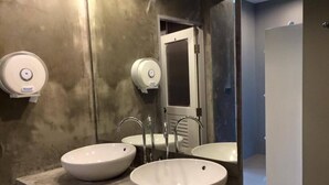 A bathroom with two large white sinks, a mirror, and two paper towel dispensers. - Hubb Hostel Phuket Airport (Sa Khu)
