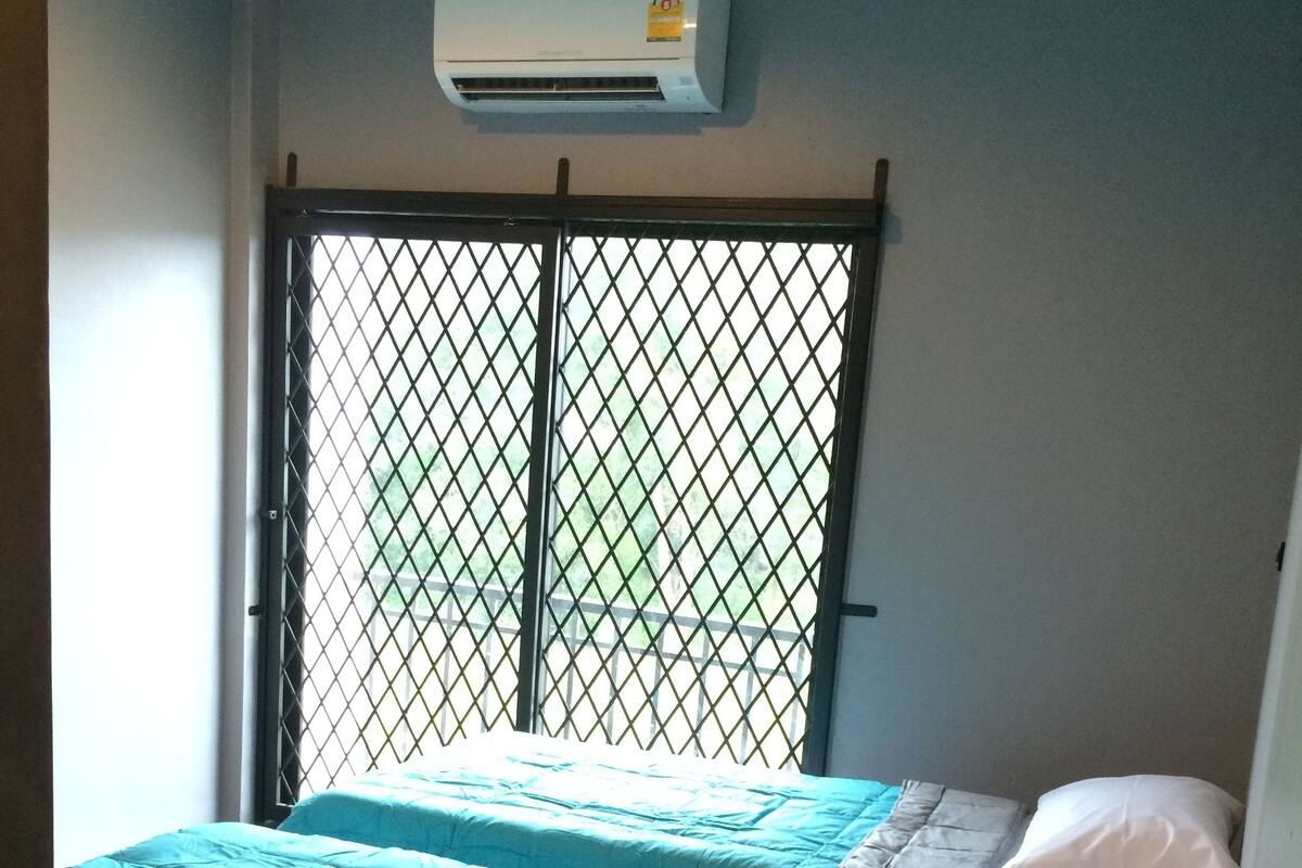 Una habitación con cama, aire acondicionado y ventana con reja.