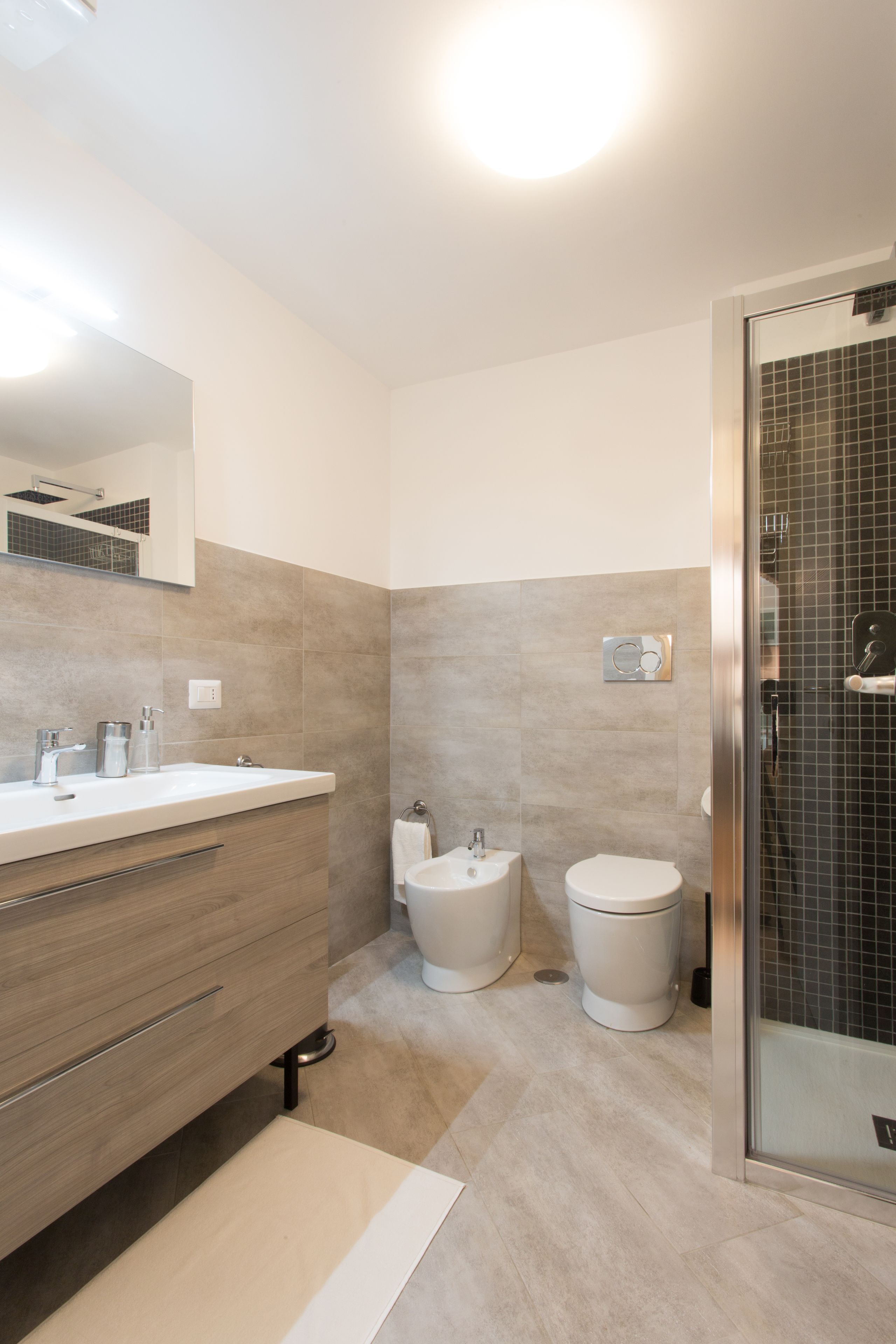 A modern bathroom with a large mirror, a sink, a toilet, and a shower area.