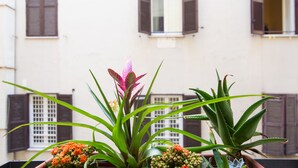 A balcony with potted plants and a building with shuttered windows in the background. - Domenichino Luxury Home (Rome)
