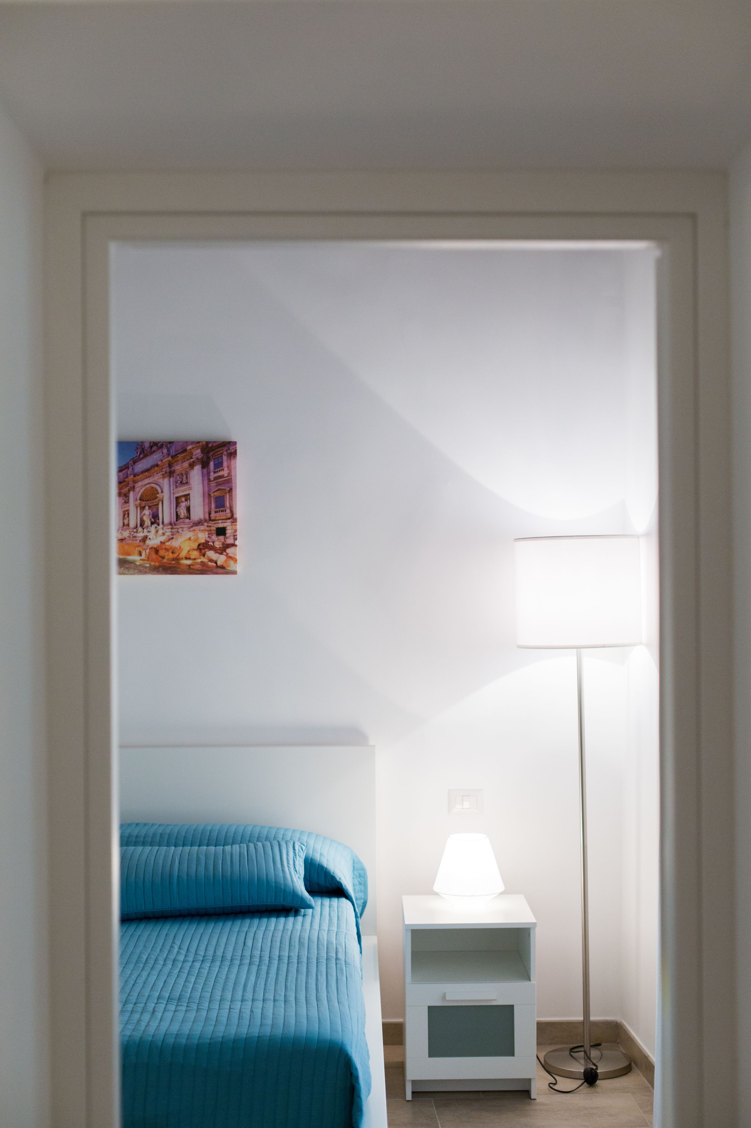 A bedroom with a bed, a bedside table with a lamp, and a wall-mounted picture.