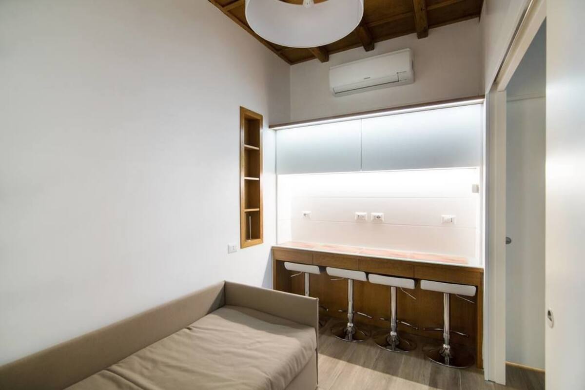 Ein kleiner, moderner Raum mit einem Bett, einem Schminktisch mit Spiegel und einem Hocker.
