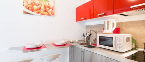 Una cocina moderna con armarios rojos, un microondas blanco y un lavamanos.