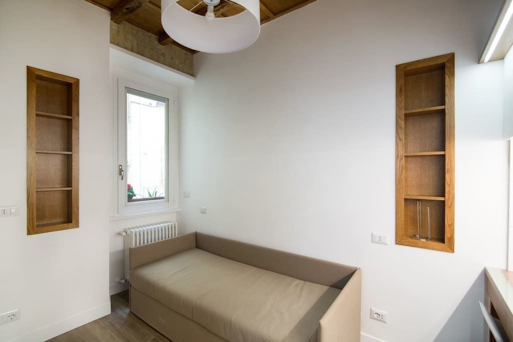 Une petite pièce lumineuse, avec une fenêtre, un radiateur et deux étagères en bois.
