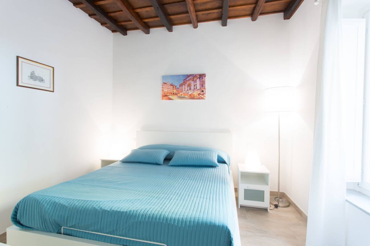 Ein Schlafzimmer mit einem Bett, einem Nachttisch, einer Stehlampe und einem gerahmten Bild an der Wand.