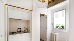 A compact kitchen with white cabinets, a kettle, and a window with a view of greenery. - Domenichino Luxury Home (Rome)