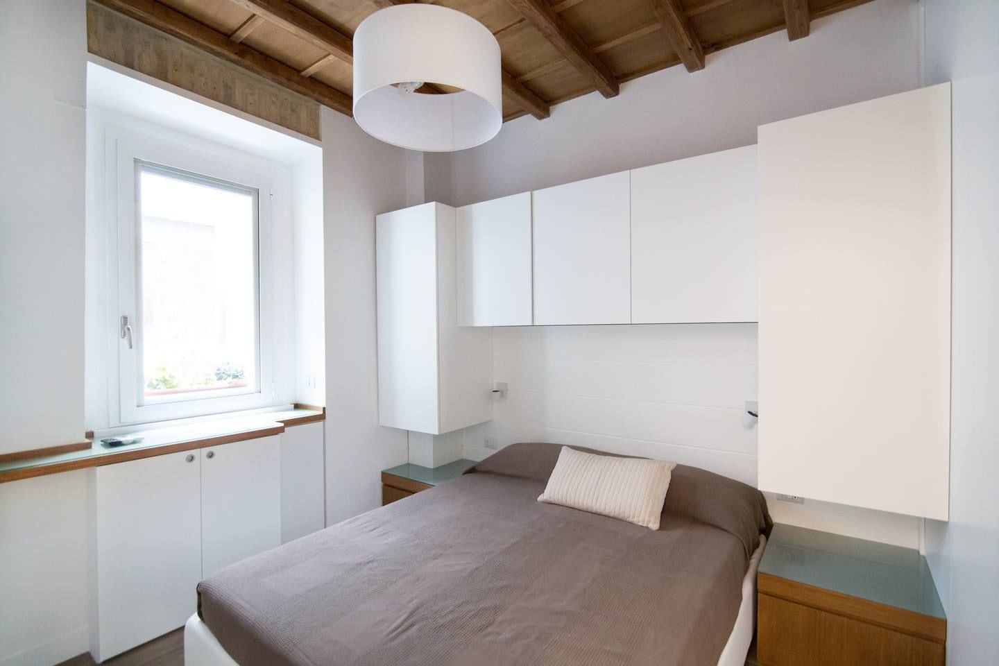 Een slaapkamer met een groot bed, een raam en ingebouwde witte kasten.