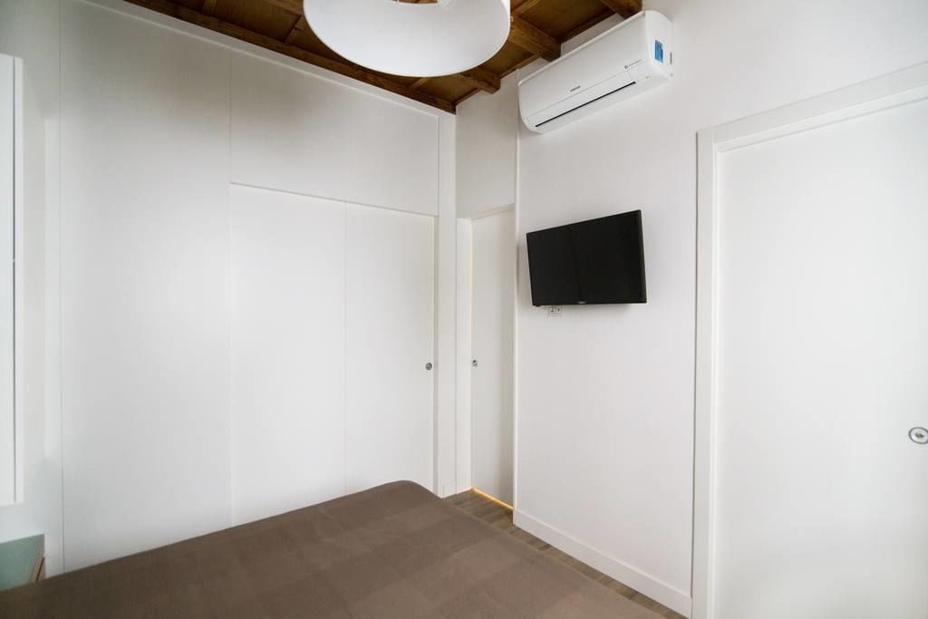 A room with white walls, a mounted TV, and an air conditioning unit.