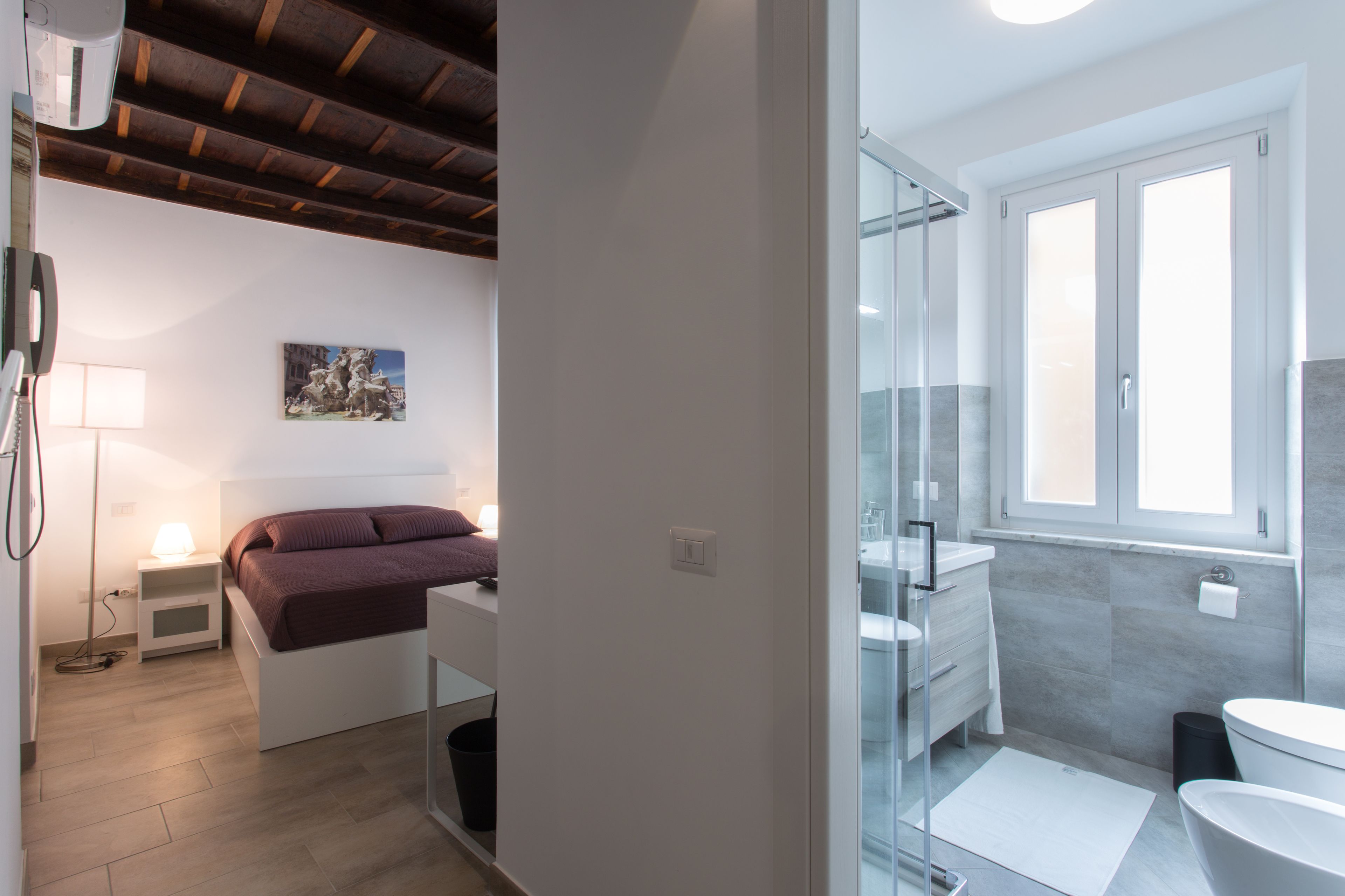 Un dormitorio con cama, mesita de noche, lámpara y un cuadro en la pared.