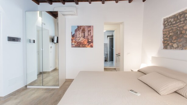 A bedroom with a bed, a mirror, a painting, and a stone wall. - Domenichino Luxury Home (Rome)