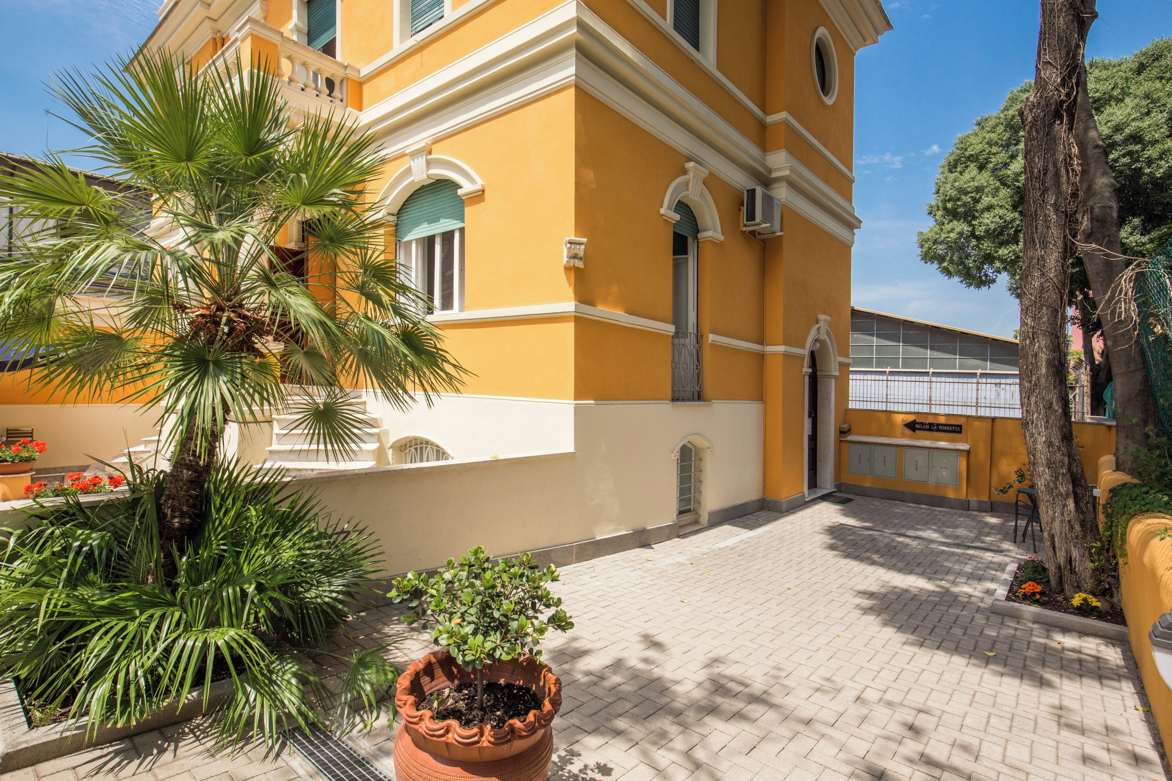 A building with a yellow facade, a palm tree, and a potted plant.