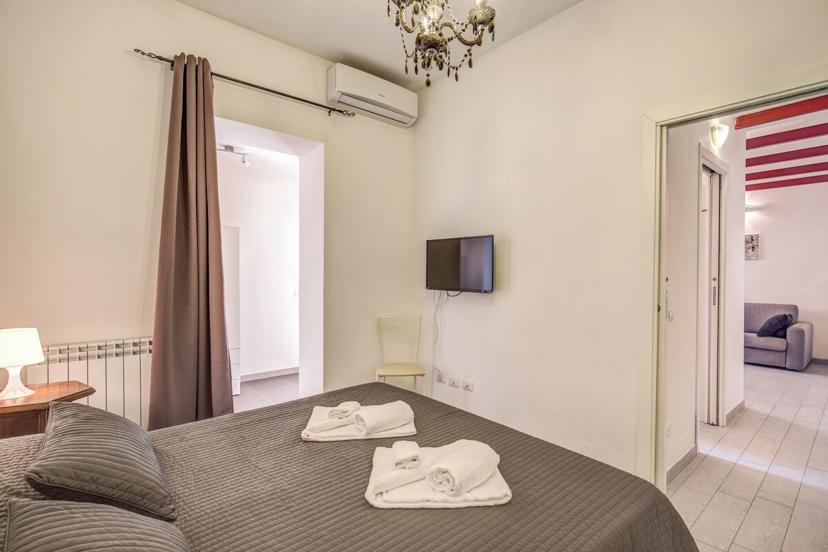 A hotel room with a bed, a TV mounted on the wall, a chair, and a door leading to a balcony.
