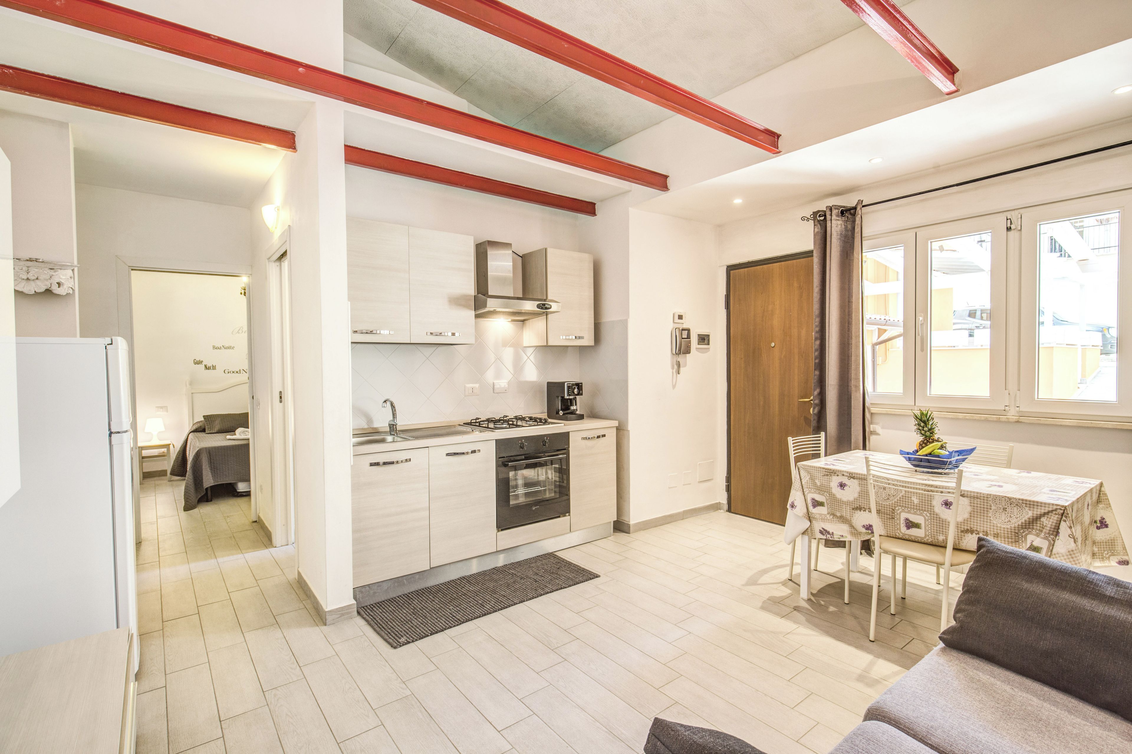 A compact kitchen with white cabinets, a stove, and a sink. There is a dining area with a table and chairs.