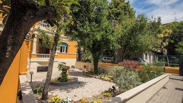 A courtyard with a palm tree, a flower bed, and a building with yellow walls.
