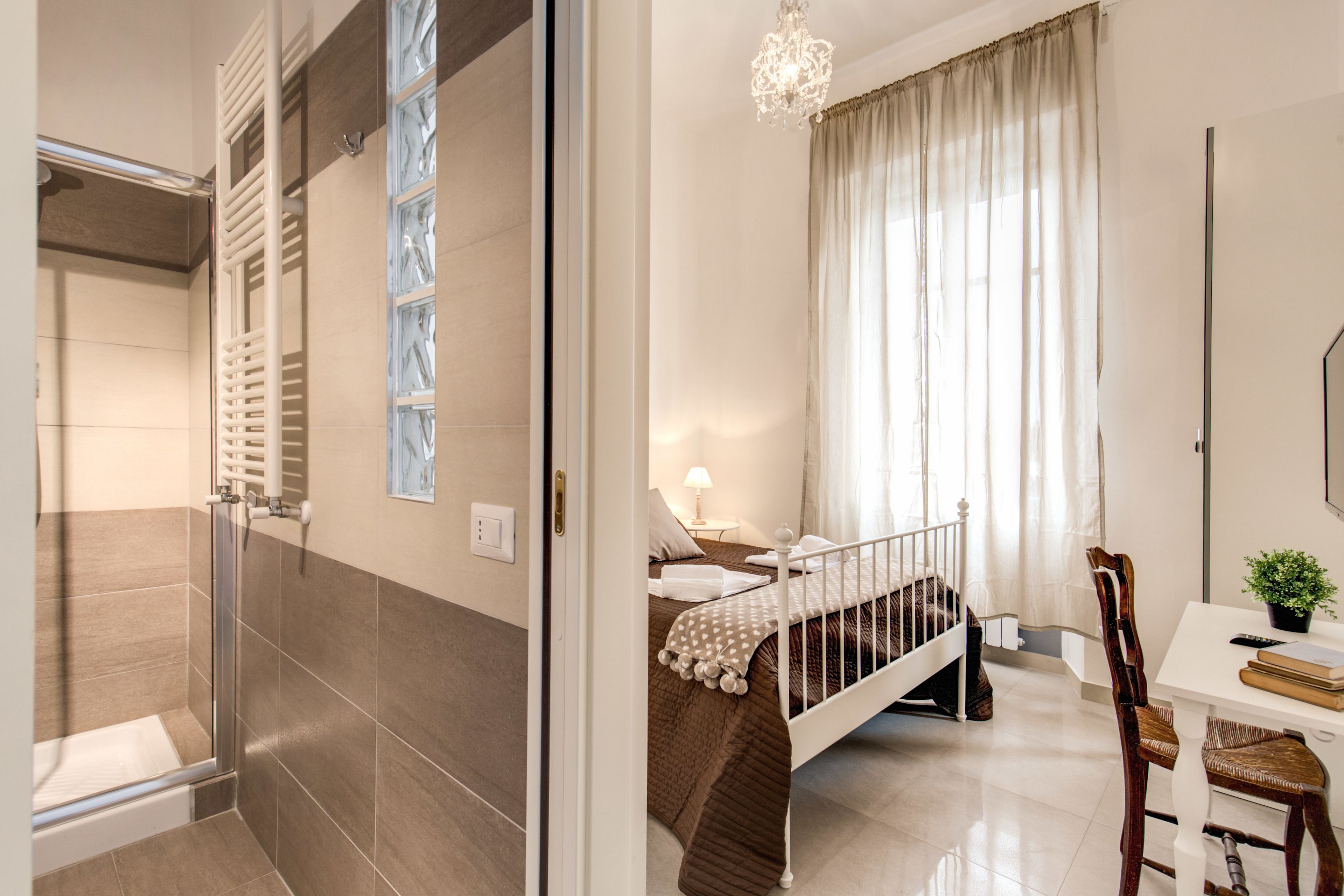 A modern hotel room with a shower, a bed with a wooden headboard, a desk with a chair, and a large window with curtains.