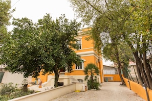 A yellow building with a staircase leading to a balcony, surrounded by trees and a paved area. - Relais La Torretta (Rome)