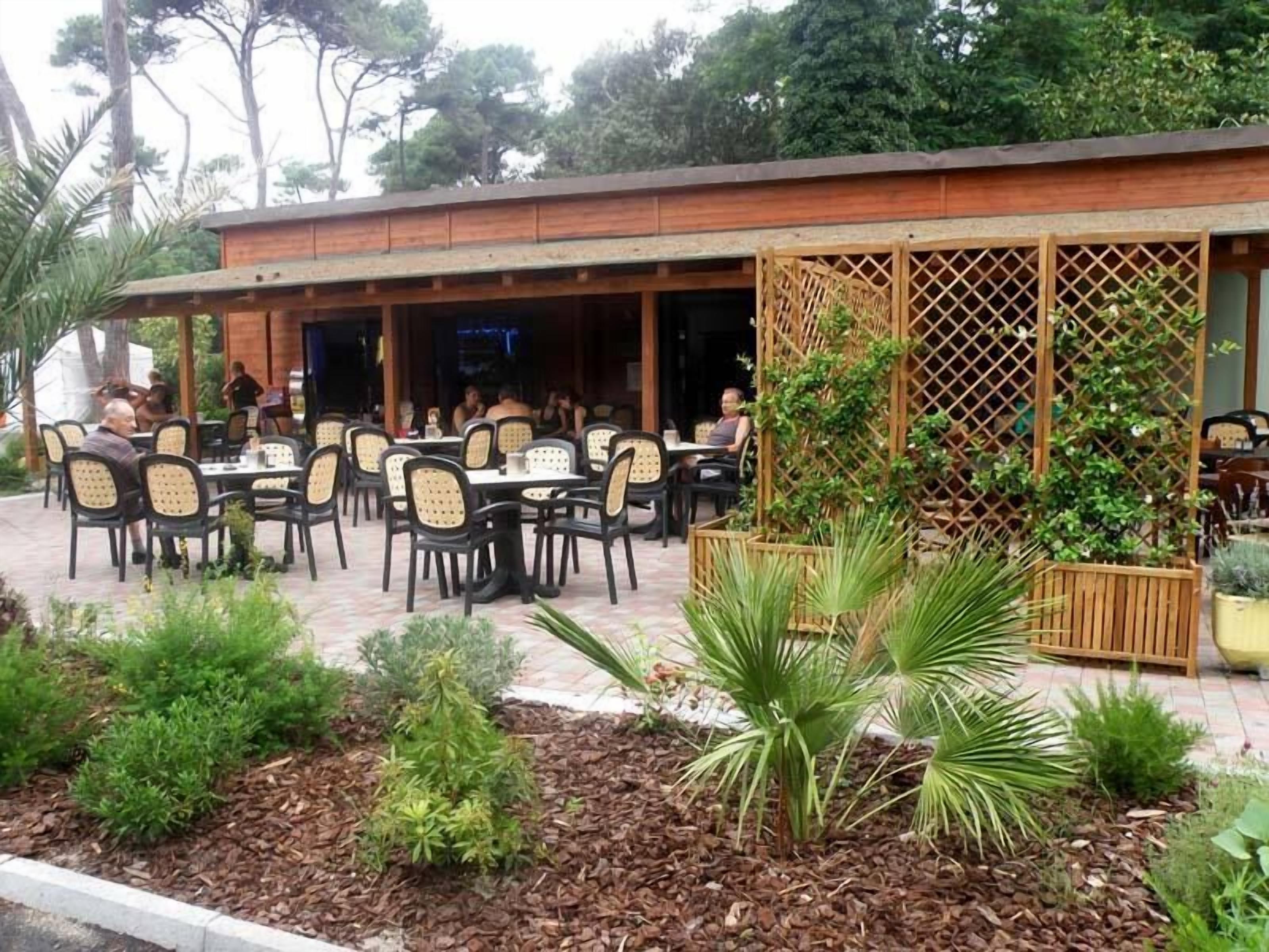 Un espace de restauration en plein air, avec des tables et des chaises, entouré de plantes et d’une clôture en bois.