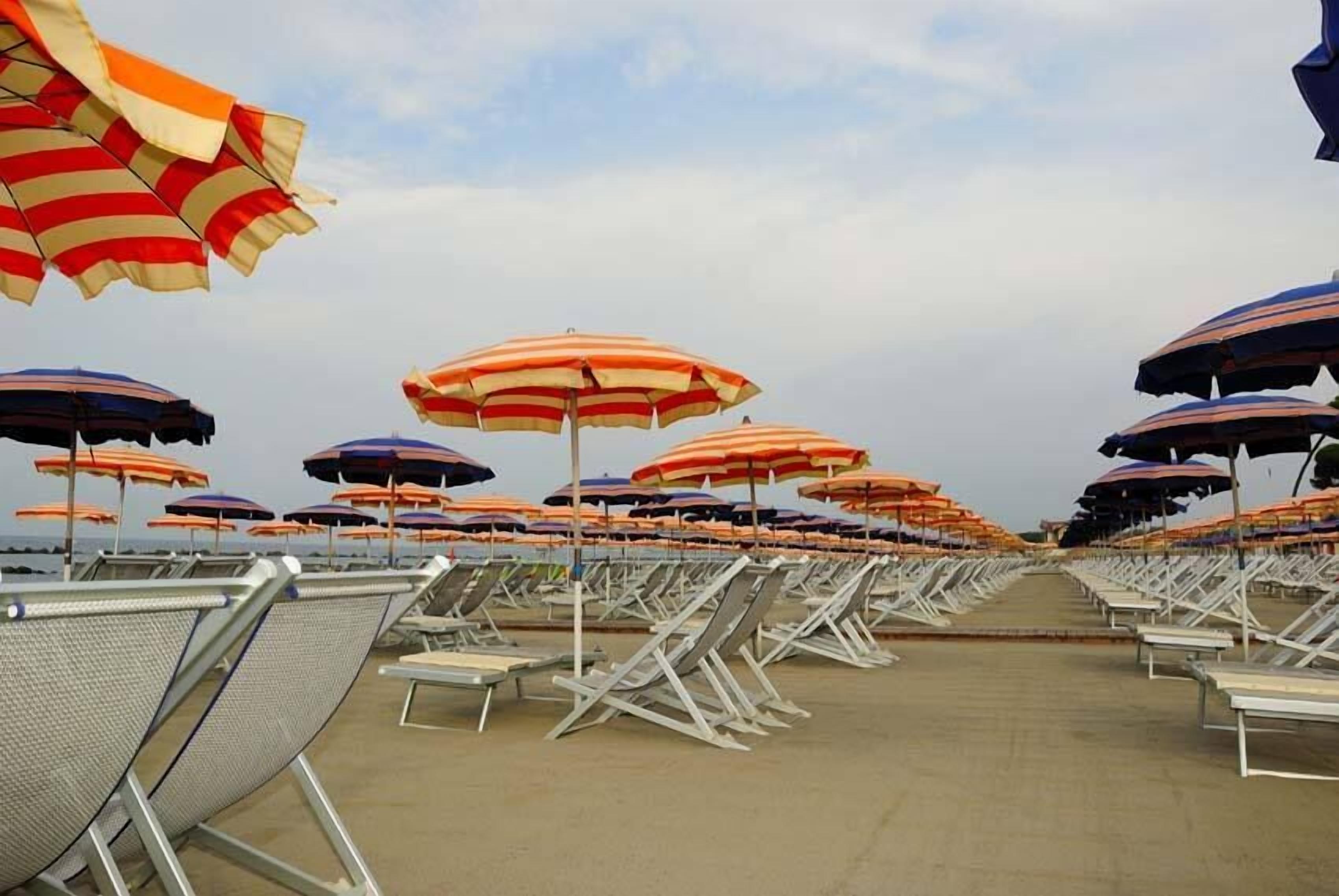 Una spiaggia con file di sdraio e ombrelloni a righe.