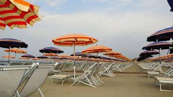 Una spiaggia con file di sdraio e ombrelloni a righe.