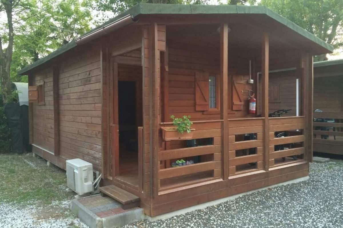 Una cabaña de madera con un porche, un extintor y un pequeño equipo de aire acondicionado.