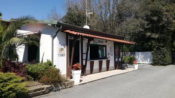 A small, single-story building with a tiled roof, a visible entrance, and a small outdoor seating area with a bench.