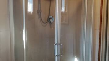 Une cabine de douche fermée par des parois de verre, dotée d’un plafond incurvé et d’une serviette blanche accrochée à la porte.