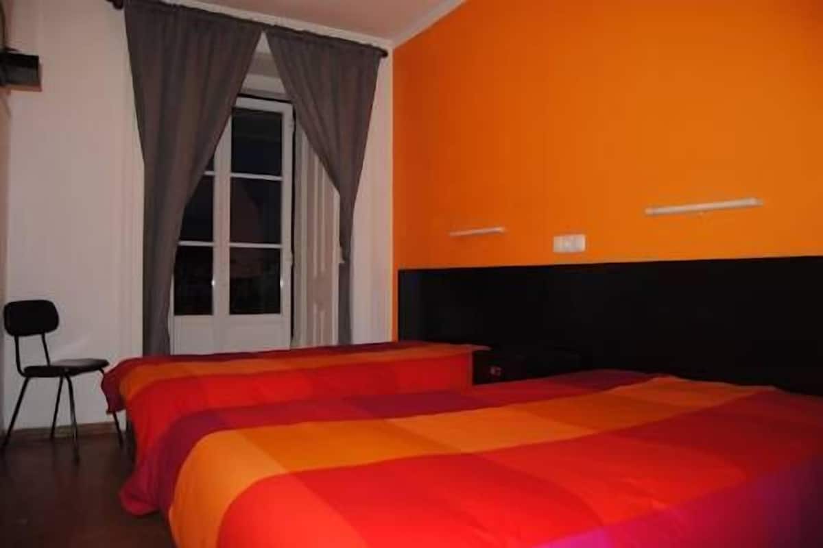 Een kamer met twee bedden, een raam met gordijnen, een stoel en een oranje wand.
