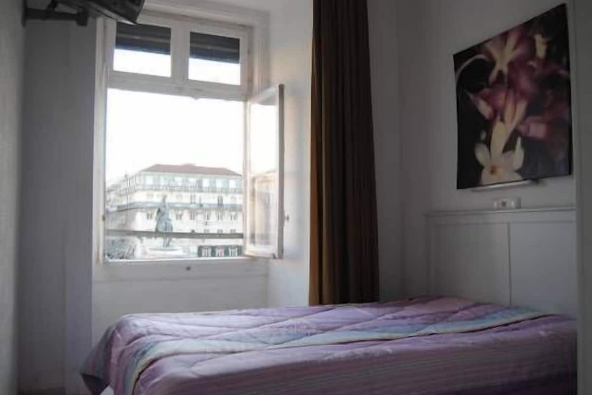 Een slaapkamer met een bed, een raam met gordijnen en een schilderij aan de muur.
