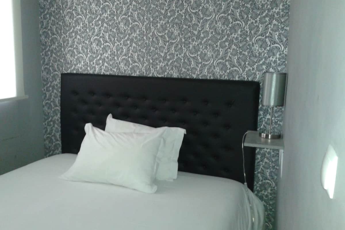 Een opgemaakt bed met een gestoffeerd hoofdeinde in een kamer met behang.