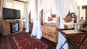 Uma cama de dossel com cortina, televisão, minibar e minibar sobre um piso de madeira com tapete estampado.