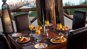 Mesa de jantar posta para o café da manhã, com frutas, suco e vista para o oceano.