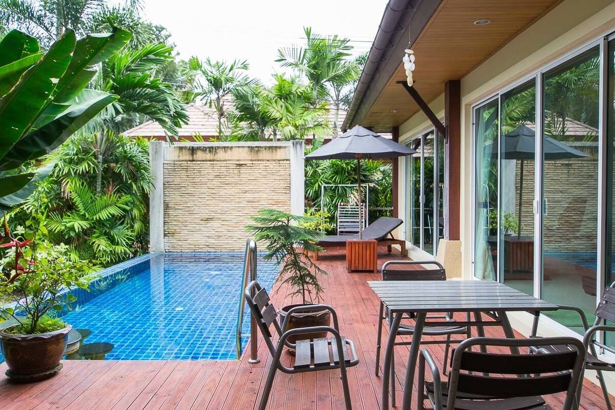 Área da piscina com deck de madeira, espreguiçadeiras e uma pequena mesa.