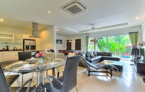 A modern living room with a glass dining table, black leather sofa, and a pool table.